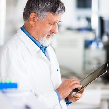 Senior doctor/scientist using his tablet computer at work (color toned image)