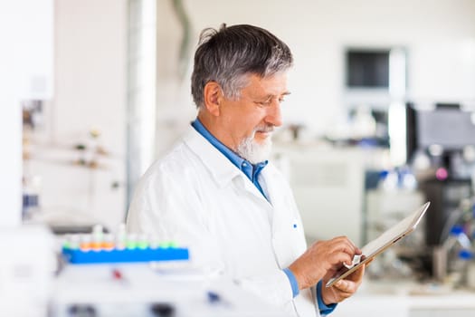 Senior doctor/scientist using his tablet computer at work (color toned image)