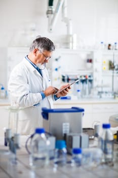 Senior doctor/scientist using his tablet computer at work (color toned image)