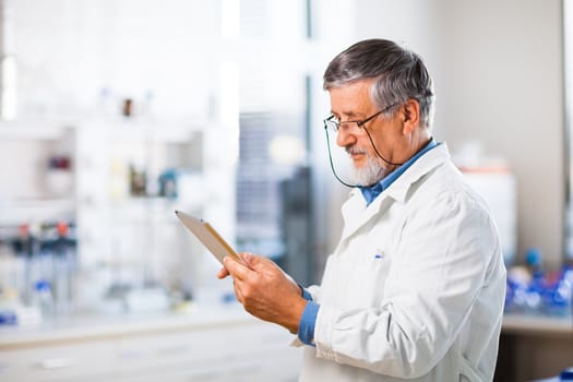 Senior doctor/scientist using his tablet computer at work (color toned image)