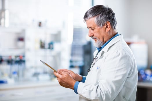 Senior doctor/scientist using his tablet computer at work (color toned image)