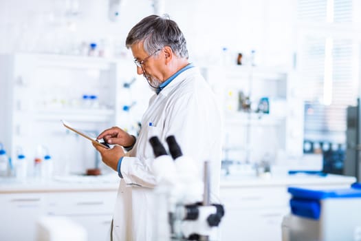 Senior doctor/scientist using his tablet computer at work (color toned image)