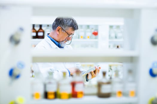 Senior doctor/scientist using his tablet computer at work (color toned image)