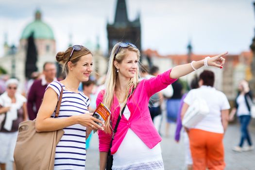 Two female tourists walking along the Charles Bridge while sightseeing in Prague, the historical capital of the Czech Republic (color toned image; shallow DOF)