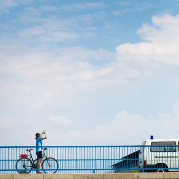 Background for poster or advertisment pertaining to cycling/sport/outdoor activities - female cyclist during a halt on a bridge against blue sky (color toned image)