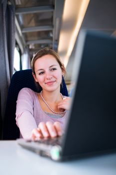 Young woman using her laptop computer while on the train (shallow DOF; color toned image)