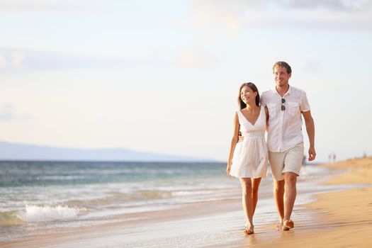 Couple walking on beach. Young happy interracial couple walking on beach smiling holding around each other. Asian woman, Caucasian man.