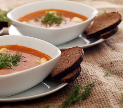 Image of bowls of hot red soup served with bread on a beige tablecloth