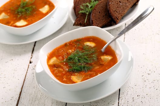 Image of bowl of hot red soup and black bread on white wooden table