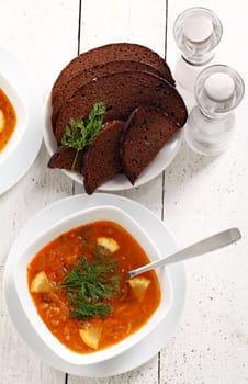 Image of bowl of hot red soup and black bread on white wooden table