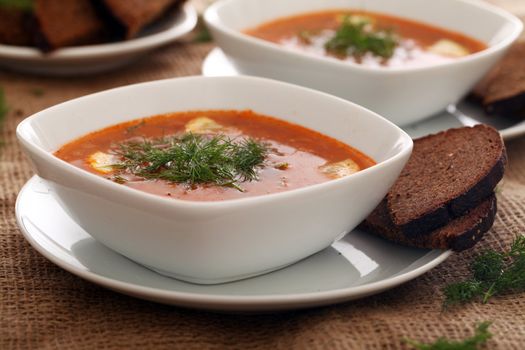 Image of bowls of hot red soup served with bread on a beige tablecloth