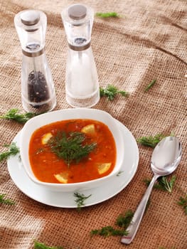 Image of bowl of hot red soup served with the salt, pepper and spoon on a beige tablecloth