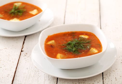 Image of two bowls of hot red soup isolated on white wooden table