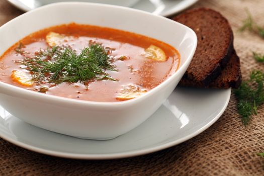 Image of bowls of hot red soup served with bread on a beige tablecloth