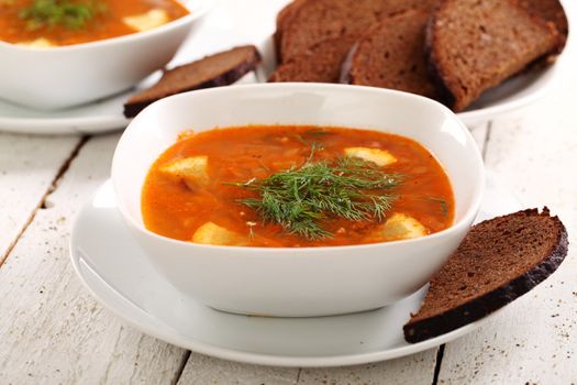 Image of bowl of hot red soup and black bread on white wooden table