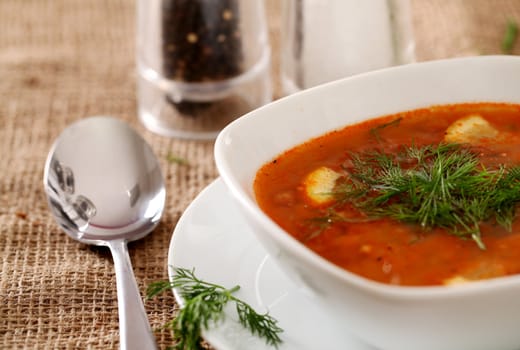 Image of bowl of hot red soup served with the salt, pepper and spoon on a beige tablecloth