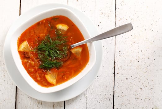 Image of bowl of hot red soup isolated on white wooden table