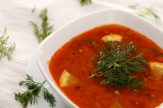 Image of bowl of hot red soup served with parsley on brown tablecloth