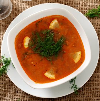 Image of bowl of hot red soup served with the salt, pepper and spoon on a beige tablecloth