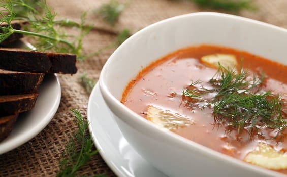 Image of bowls of hot red soup served with bread on a beige tablecloth