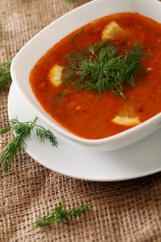 Image of bowl of hot red soup served with parsley on a beige tablecloth