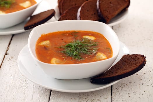 Image of bowl of hot red soup and black bread on white wooden table