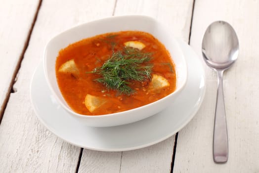 Image of bowl of hot red soup isolated on white wooden table