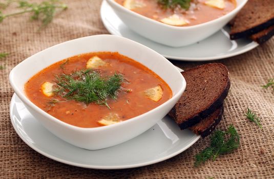 Image of bowls of hot red soup served with bread on a beige tablecloth