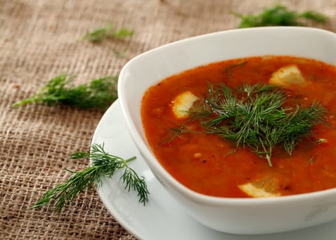 Image of bowl of hot red soup served with parsley on a beige tablecloth