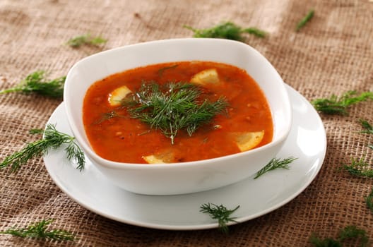 Image of bowl of hot red soup served with parsley on a beige tablecloth