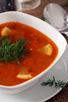 Image of bowl of hot red soup served with the salt, pepper and spoon on a beige tablecloth