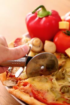 Fresh italian pizza in plate being sliced with pizza knife on a wooden surface