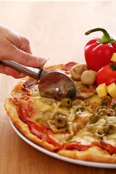 Fresh italian pizza in plate being sliced with pizza knife on a wooden surface