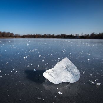 Freezing winter temperatures: block of ice lying on the surface of a frozen pond on a sunny winter day