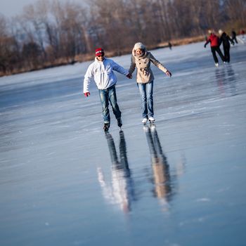 Couple ice skating outdoors on a pond on a lovely sunny winter day