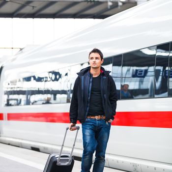 Just arrived: handsome young man walking along a platform at a modern train station