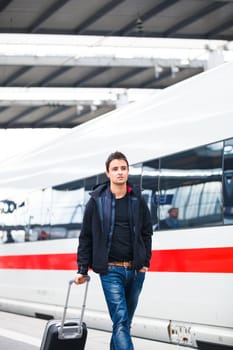 Just arrived: handsome young man walking along a platform at a modern train station