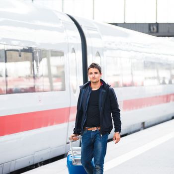 Just arrived: handsome young man walking along a platform at a modern train station