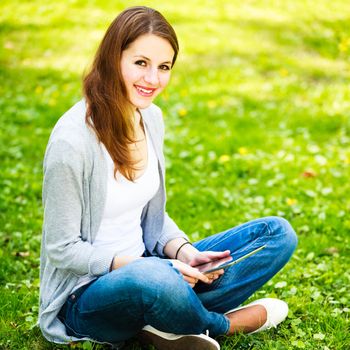 Young woman using her tablet computer while relaxing outdoors in a park on a lovely spring day