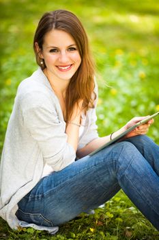 Young woman using her tablet computer while relaxing outdoors in a park on a lovely spring day