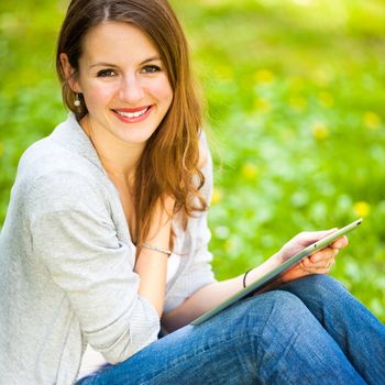 Young woman using her tablet computer while relaxing outdoors in a park on a lovely spring day