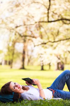 Young woman using her tablet computer while relaxing outdoors in a park on a lovely spring day