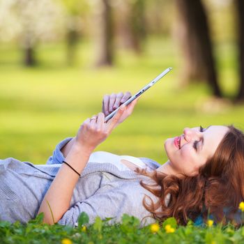 Young woman using her tablet computer while relaxing outdoors in a park on a lovely spring day