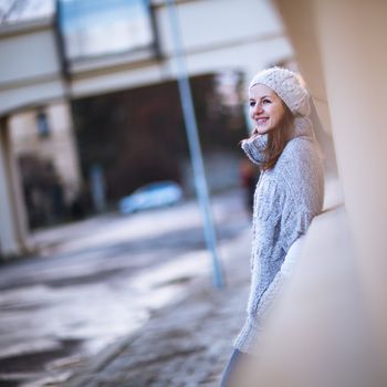 Autumn/winter portrait: young woman dressed in a warm woolen cardigan posing outside in a city park