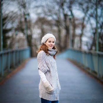 Autumn/winter portrait: young woman dressed in a warm woolen cardigan posing outside in a city park