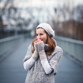 Autumn/winter portrait: young woman dressed in a warm woolen cardigan posing outside in a city park