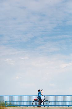 Background for poster or advertisment pertaining to cycling/sport/outdoor activities - female cyclist during a halt on a bridge against blue sky (color toned image)