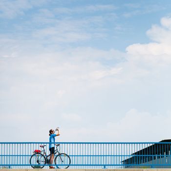 Background for poster or advertisment pertaining to cycling/sport/outdoor activities - female cyclist during a halt on a bridge against blue sky (color toned image)