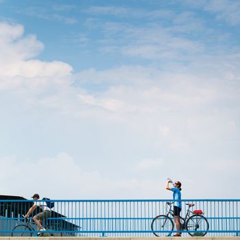 Background for poster or advertisment pertaining to cycling/sport/outdoor activities - female cyclist during a halt on a bridge against blue sky (color toned image)