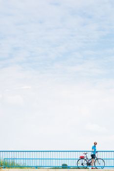 Background for poster or advertisment pertaining to cycling/sport/outdoor activities - female cyclist during a halt on a bridge against blue sky (color toned image)